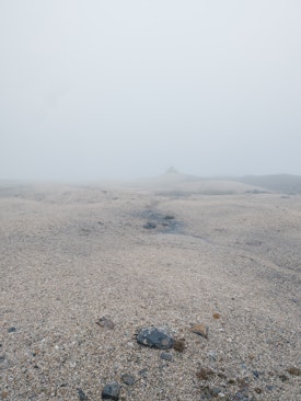A featureless landscape in the mist with a barely visible cairn